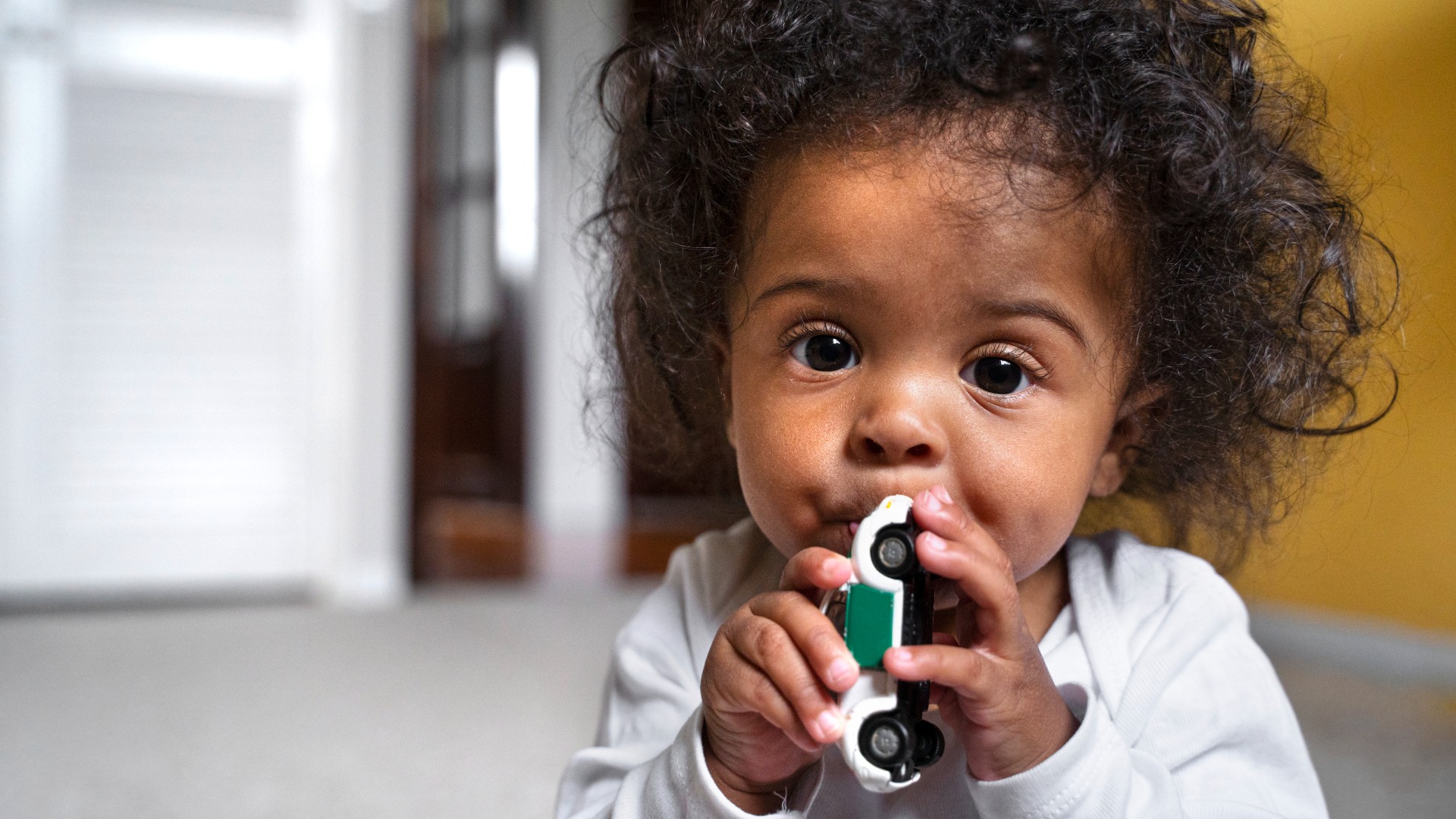 cute baby chewing on toy car while teething